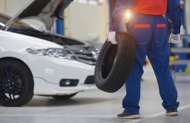 Mechanic holding a tire with a white car in the background Mechanic holding a tire with a white car in the background
