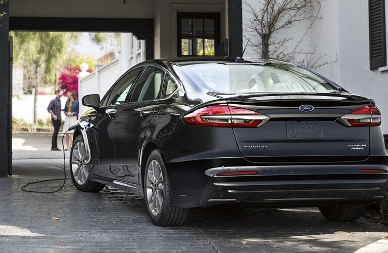 Rear driver angle of a black 2020 Ford Fusion plug-in hybrid charging at a home