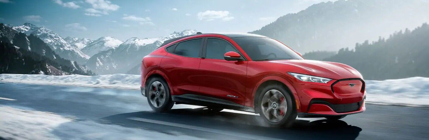 Front passenger angle of a red 2021 Ford Mustang Mach-E driving during winter