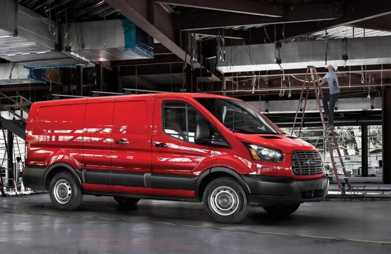 Front passenger angle of a red 2019 Ford Transit parked in a factory