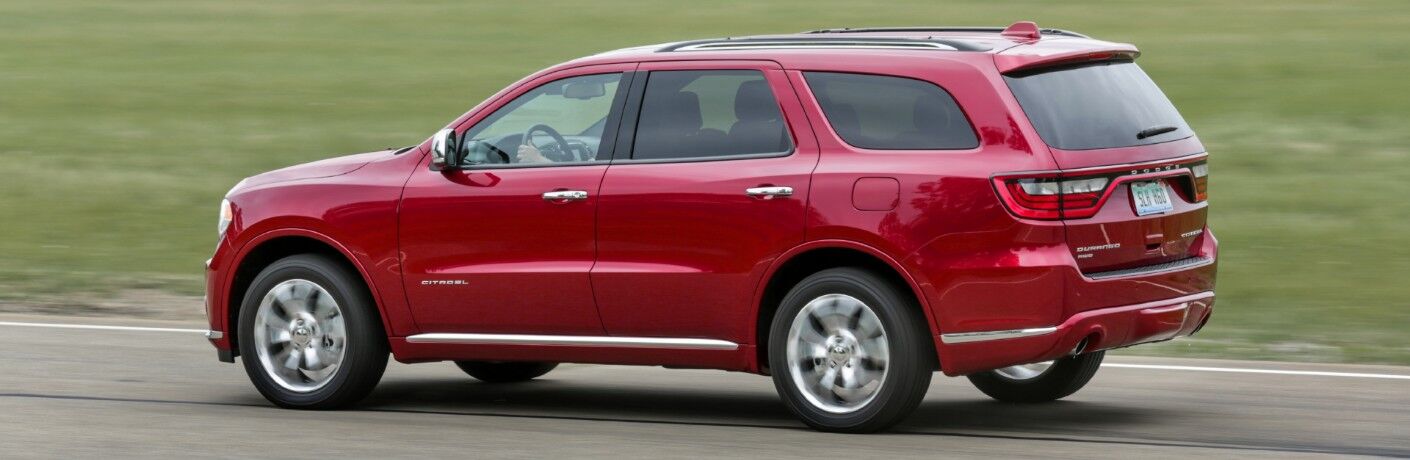 2020 Dodge Durango Citadel with AWD exterior side shot with red paint color driving near a field of grass