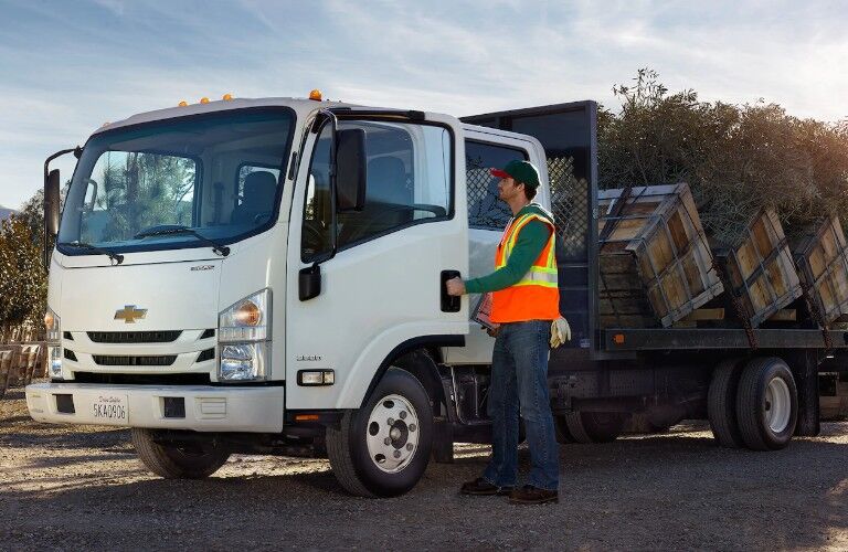Front driver angle of a white 2019 Chevrolet Low Cab Forward with plants loaded in the back and a worker getting inside