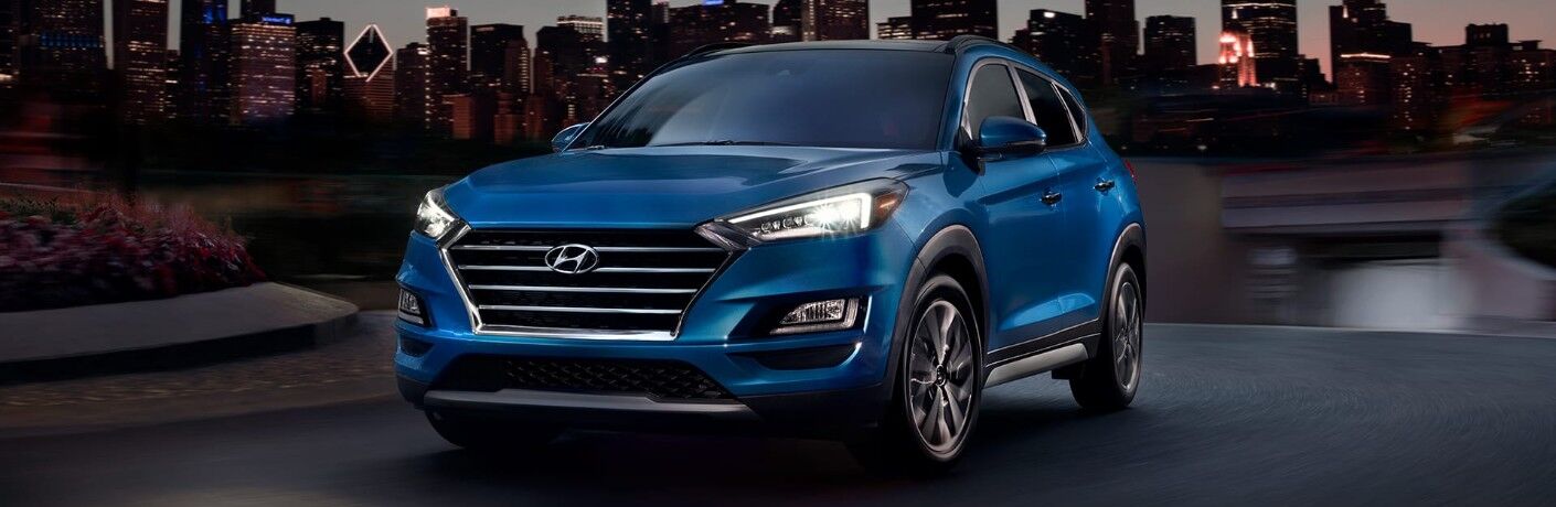 Front driver angle of a blue 2020 Hyundai Tucson with a city skyline in the background