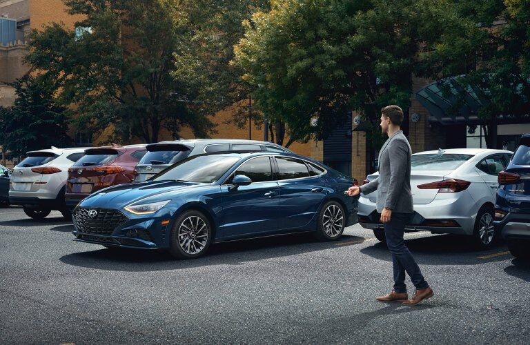 A blue 2020 Hyundai Sonata pulling out of a parking spot with a man holding his key fob nearby