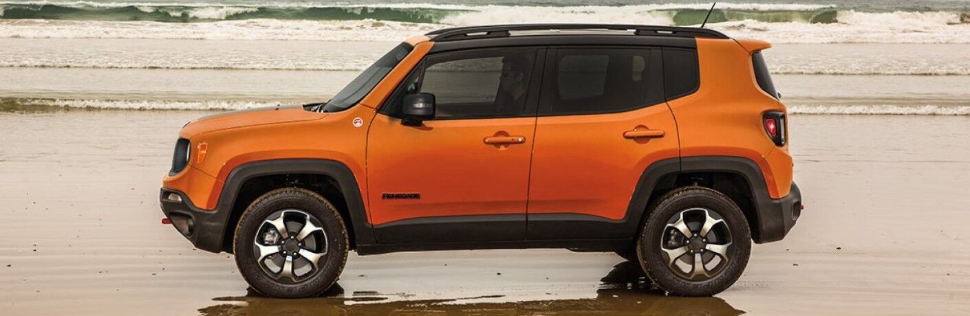 2019 Jeep Renegade exterior side shot with orange paint color parked on a beach at low tide as small waves crash