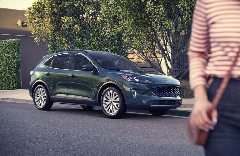 Front passenger angle of a green 2020 Ford Escape parked on the side of a street and a woman walking away from it