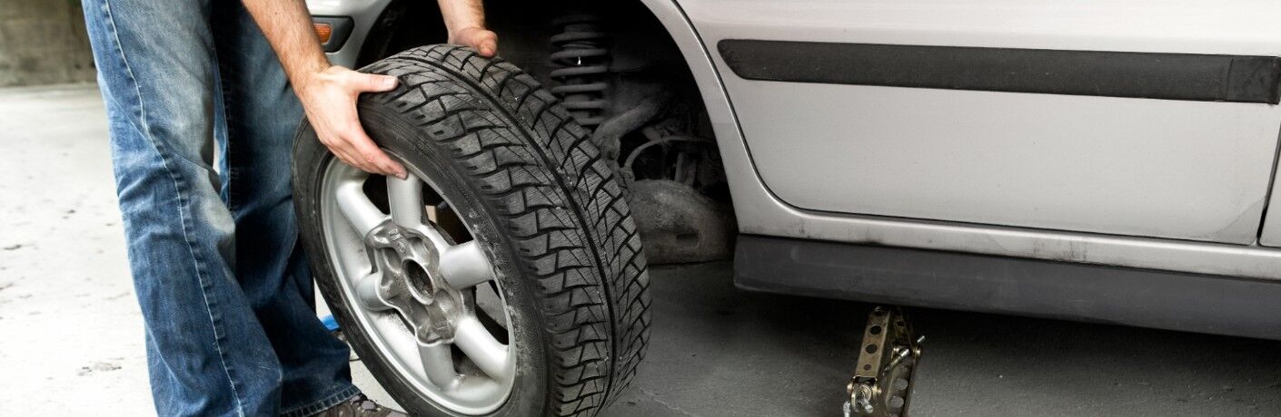 Person holding a tire by a car