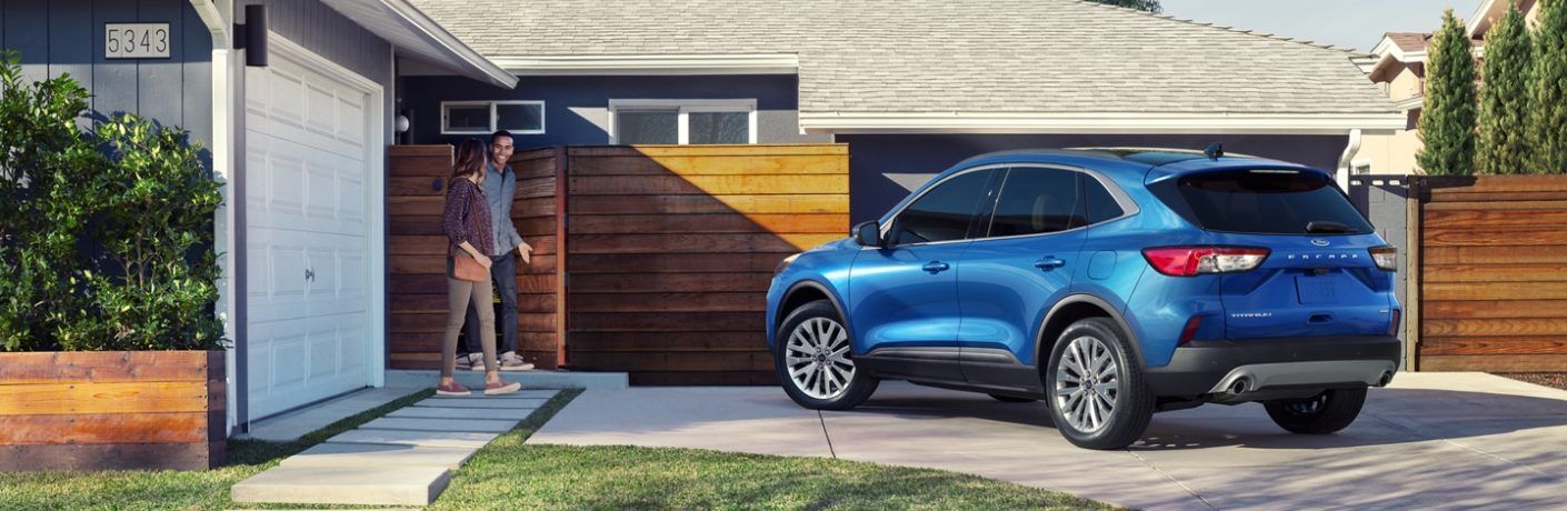 Rear driver angle of a blue 2020 Ford Escape parked in a driveway with a couple walking out of their home towards it