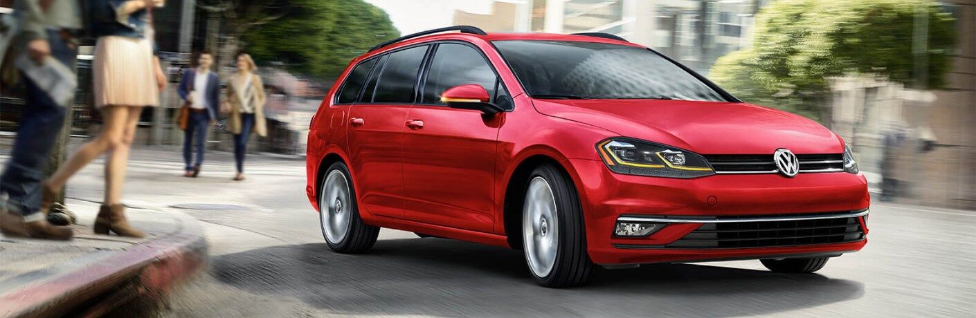 Front passenger angle of a red 2019 Volkswagen Golf SportWagen driving on a curvy city road