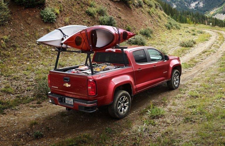 Rear passenger angle of a red 2020 Chevy Colorado with the truck bed loaded and two kayaks secured on top