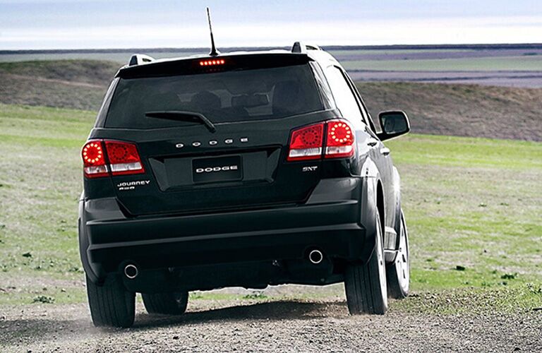 2019 Dodge Journey exterior shot with black paint color driving on a gravel road in a forest as dust kicks up from the wheels