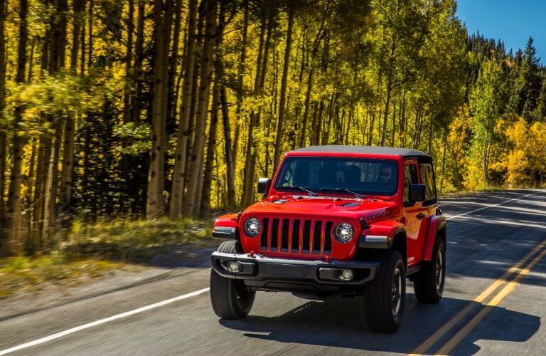 2020 Jeep Wrangler Rubicon exterior shot with firecracker red paint color driving alongside a forest under the sun
