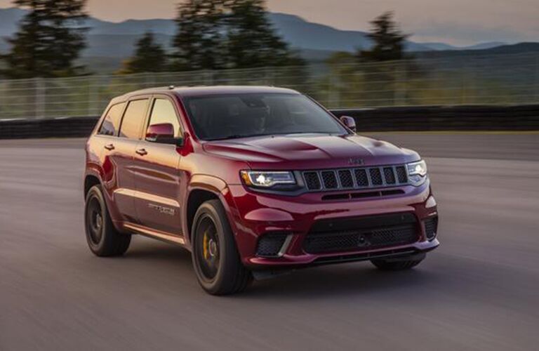 2020 Jeep Grand Cherokee red paint driving on road with fence in background and trees and mountains twilight hour