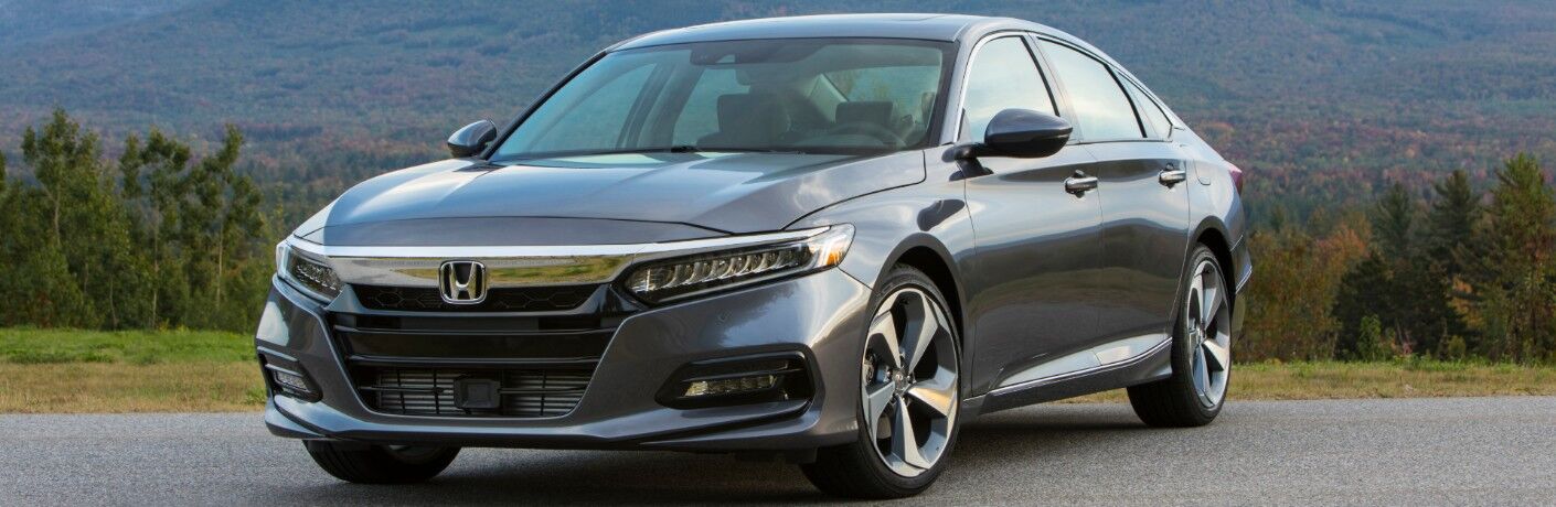 2020 Honda Accord Touring exterior shot with gray metallic paint color parked on an asphalt walking path with a background of forest trees and mountain hills