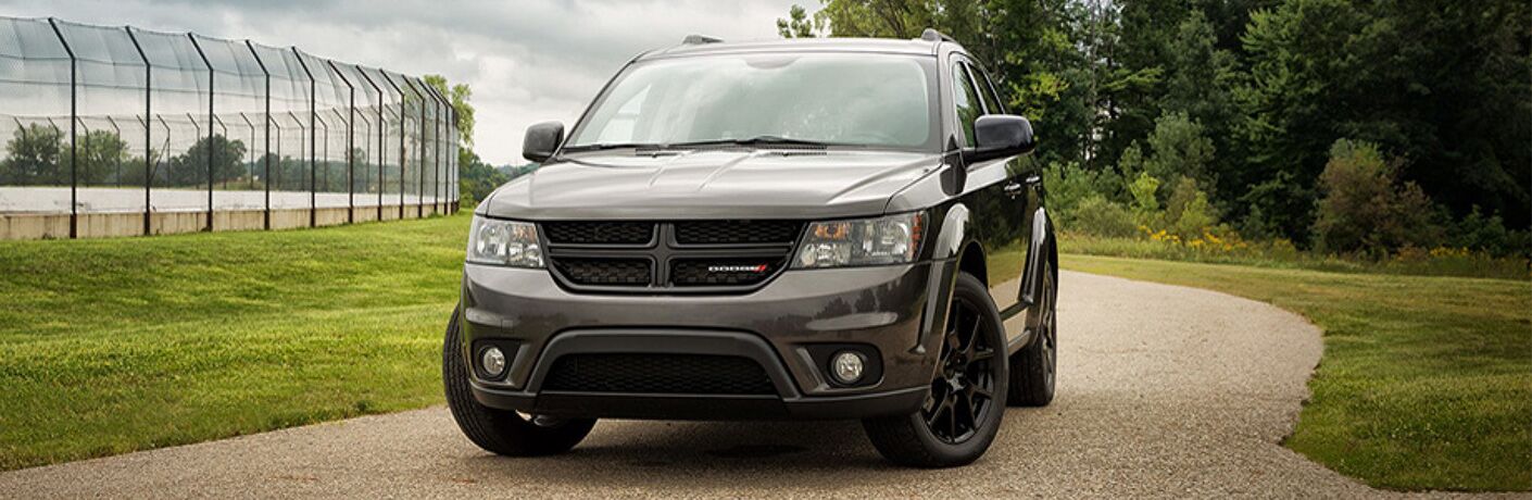 2019 Dodge Journey exterior front shot with black paint color parked on a gravel path outside a baseball field and net