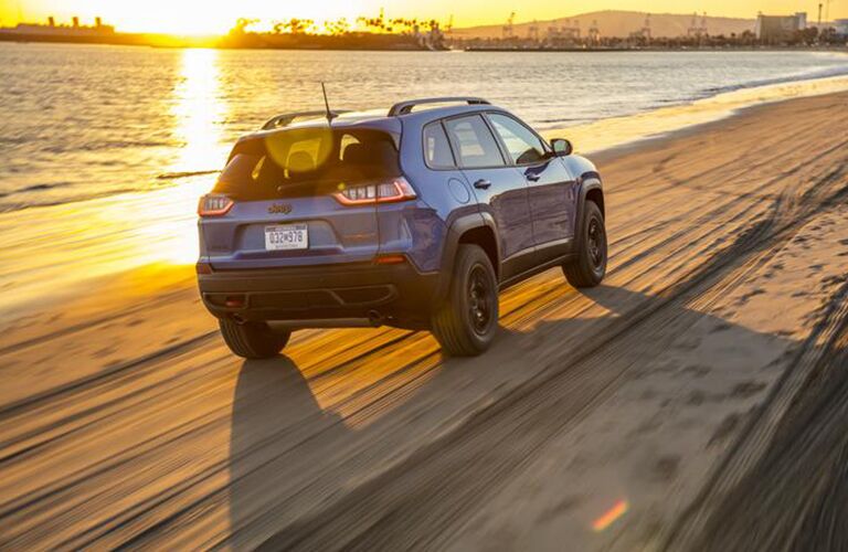 2020 Jeep Cherokee exterior rear shot driving on the beach coast near the water as the sun glares