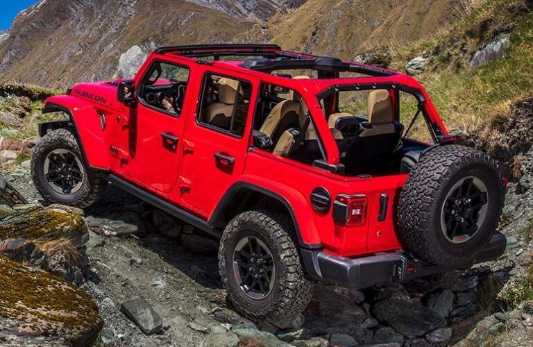 2020 Jeep Wrangler exterior rear side shot with firecracker red paint color driving off-road on rocky terrain