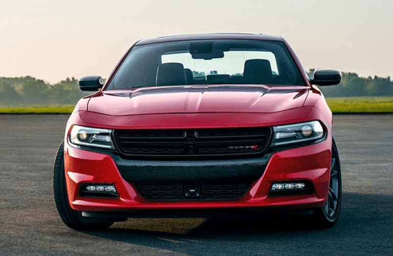 2019 Dodge Charger exterior front shot with red paint color parked on an empty lot in a grass field