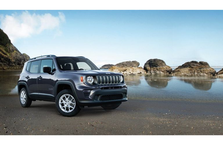 2019 Jeep Renegade exterior shot with gray paint color parked on a mud beach next to rocky cliffs and a blue sky