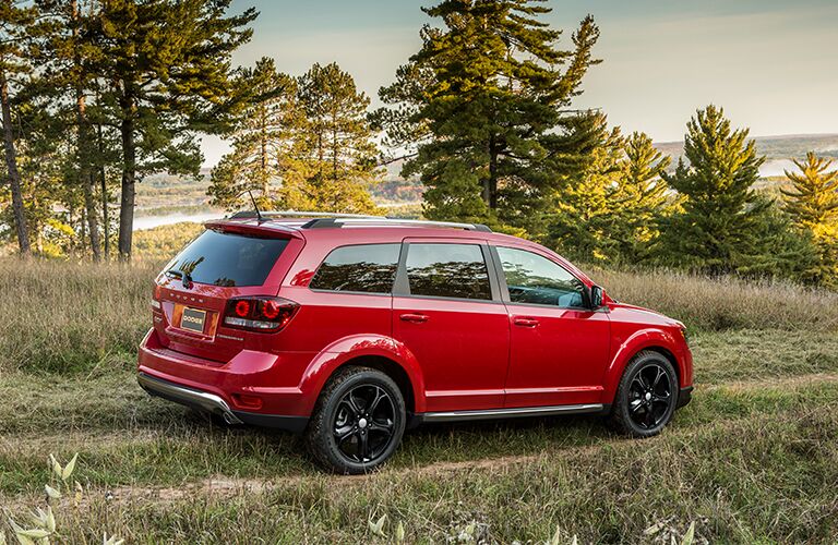 2018 Dodge Journey exterior side shot with red paint color driving off road on grass near rivers and forests