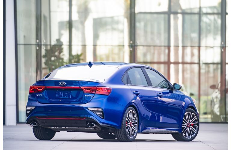 2020 Kia Forte GT exterior rear shot with blue paint color parked outside the glass walls of a car dealership