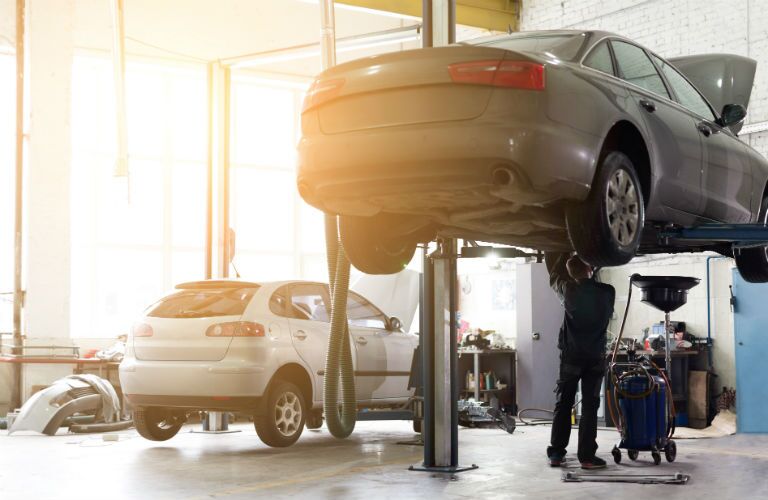 car in air with mechanic underneath changing oil