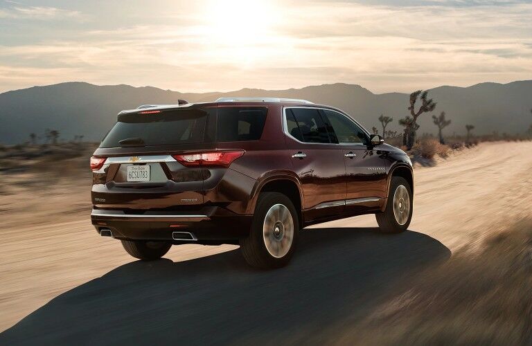 Rear passenger angle of a burgundy 2020 Chevrolet Traverse driving down a rural road