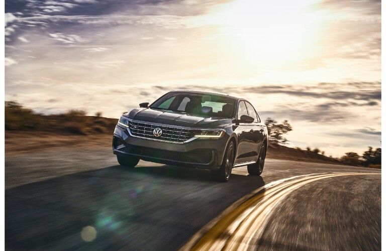 2020 Volkswagen Passat exterior front shot driving over a hill as the sun shines bright in the sky behind it