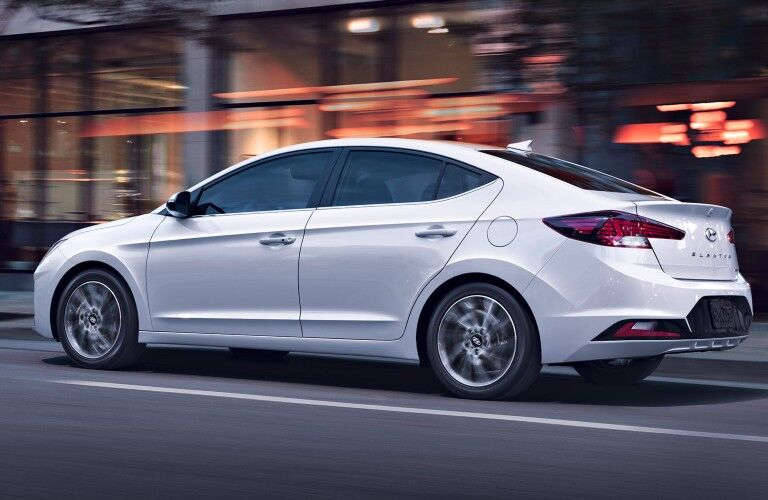 Rear driver angle of a white 2020 Hyundai Elantra driving in a city