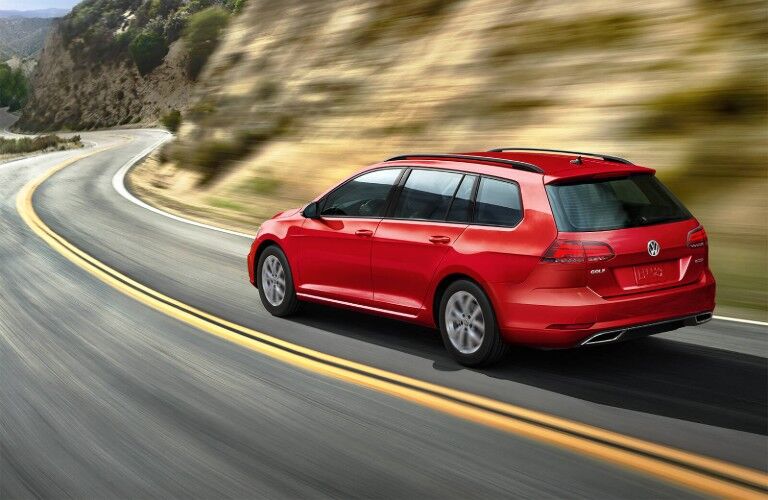 Rear driver angle of a red 2019 Volkswagen Golf SportWagen driving on a road