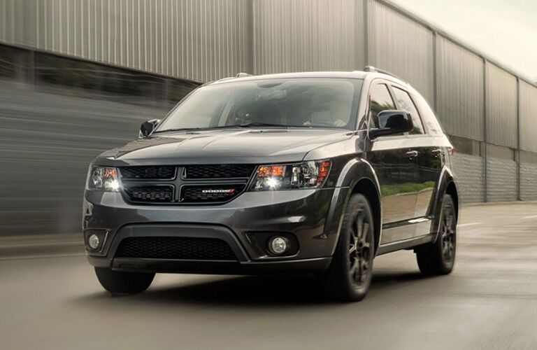 2019 Dodge Journey exterior front shot with black paint color and headlights on driving by a brick hangar