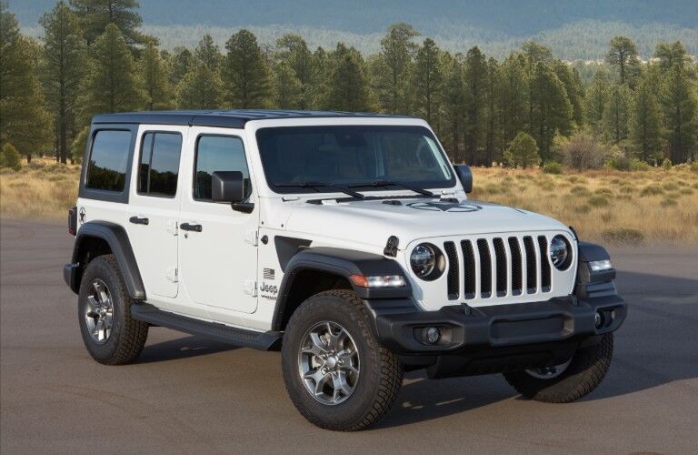 2020 Jeep Wrangler Freedom Edition with white clear coat paint color parked on an empty lot near a forest of pine trees
